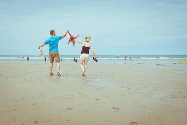 Vue arrière de parents ludiques balançant leur enfant sur la plage contre le ciel