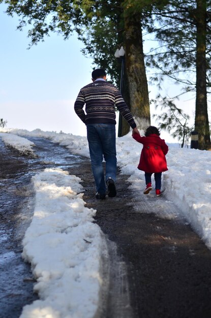 Photo vue arrière d'un père et d'une fille marchant sur un paysage couvert de neige