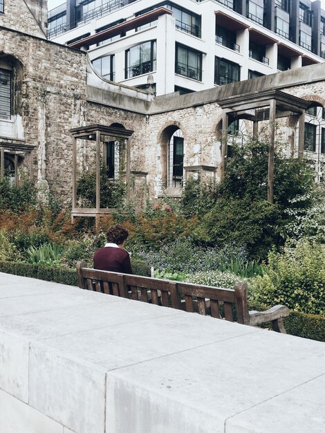 Photo vue arrière d'une personne assise sur un banc près du bâtiment