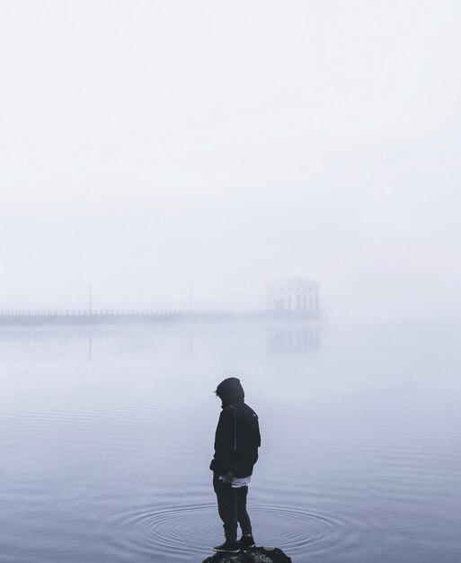 Photo vue arrière d'une personne debout dans le lac par temps brumeux