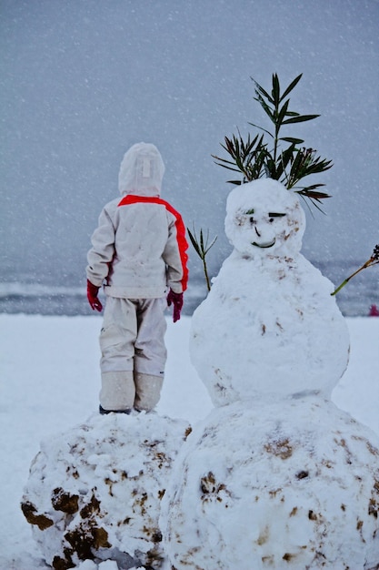 Photo vue arrière d'une personne debout près du bonhomme de neige pendant l'hiver contre le ciel