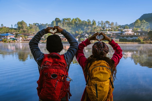 Photo vue arrière de personnes faisant une forme de cœur avec les mains alors qu'elles se tiennent au bord du lac contre le ciel