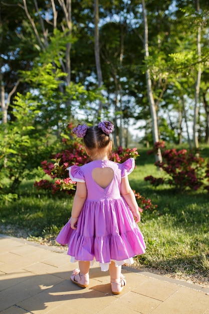 Vue arrière d'une petite fille enfant en robe d'été marchant dans un parc verdoyant