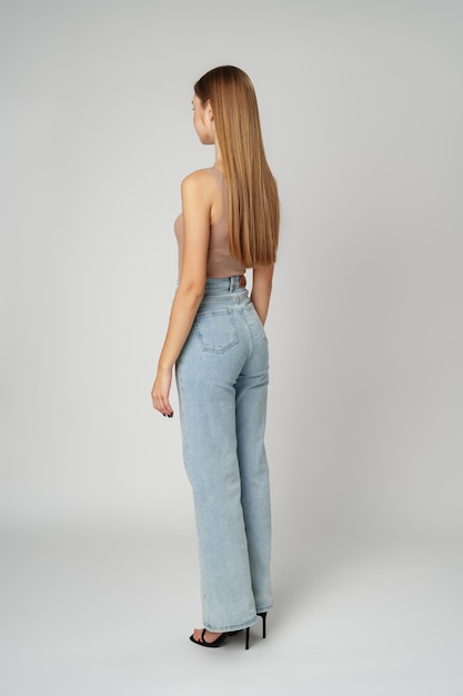 Vue arrière photo en pleine longueur d'une jeune femme aux cheveux longs sur fond gris