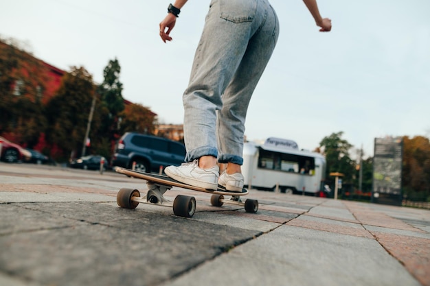 Vue arrière photo recadrée d'une skateuse à cheval sur une longue planche sur un trottoir en béton