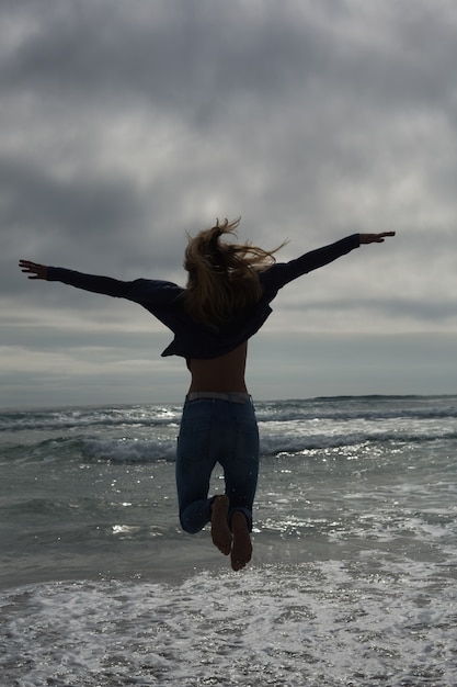 Vue arrière pleine longueur d&#39;une femme sautant à la plage