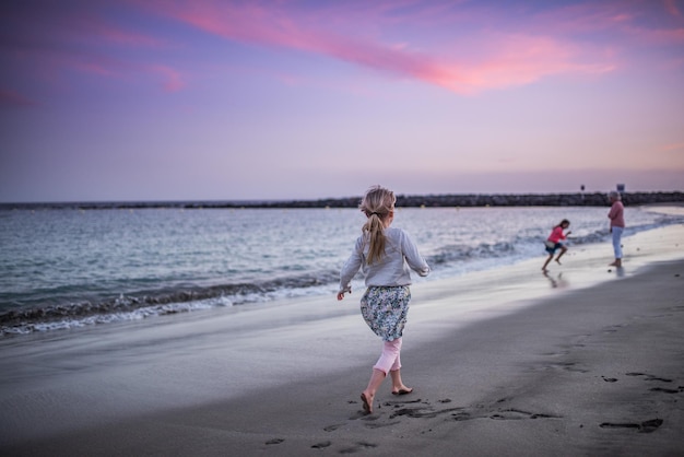 Vue arrière pleine longueur de la fille marchant sur la plage au coucher du soleil