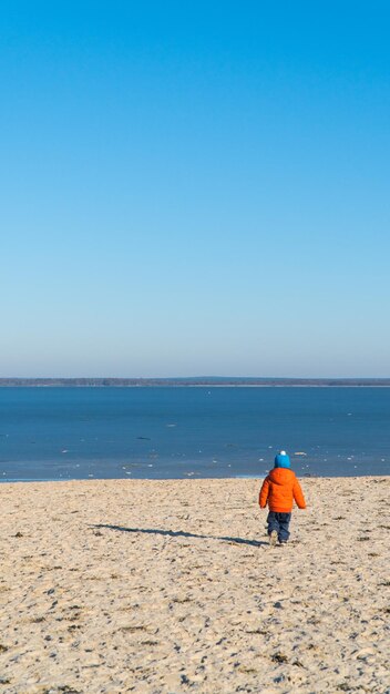 Vue arrière pleine longueur d'un garçon marchant sur la plage contre un ciel bleu clair