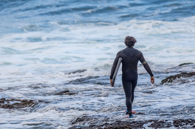Vue arrière pleine longueur d'un homme en combinaison de plongée tenant une planche de surf en mer