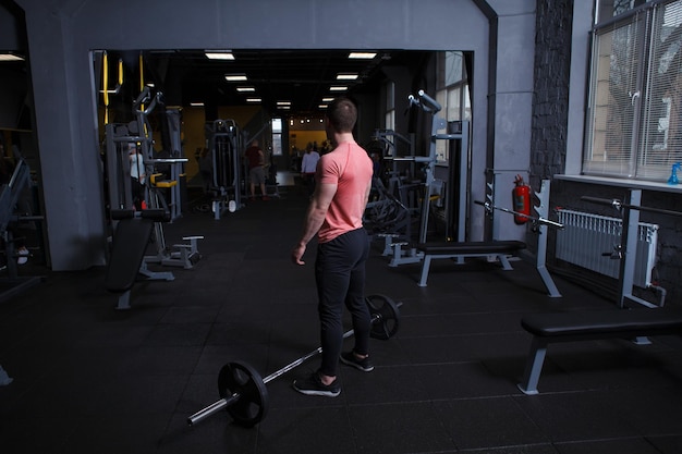 Vue arrière pleine longueur d'un sportif musclé debout devant une barre à la salle de gym