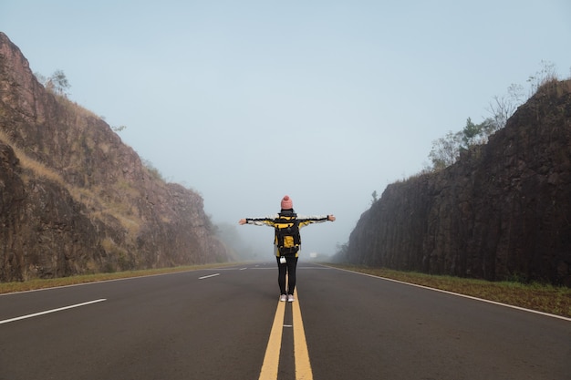 Vue arrière d'un randonneur marchant au milieu du chemin pavé avec ses bras tendus.