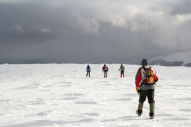 Vue arrière des randonneurs marchant sur la colline couverte de neige dans les montagnes d'hiver.