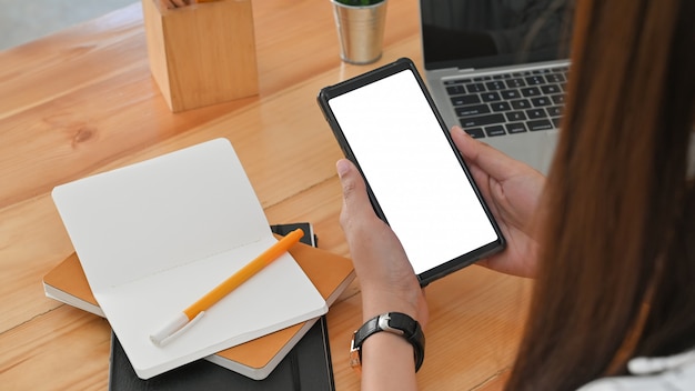 Vue arrière recadrée coup de jeune femme tout en utilisant un smartphone à écran blanc blanc sur le bureau au bureau.