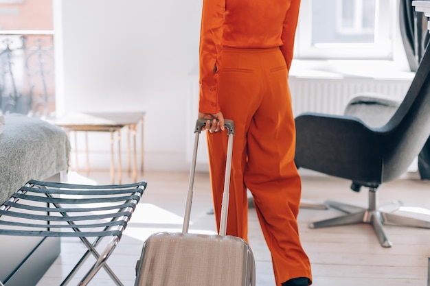 Vue arrière de la section médiane d'une femme en tenue vestimentaire élégante orange arrivant dans la chambre d'hôtel avec concept de voyage d'affaires avec bagages