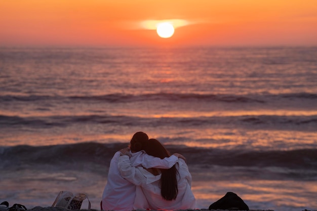 Vue arrière d'une silhouette de couple assis câlins et profitant du coucher du soleil à l'extérieur sur la plage