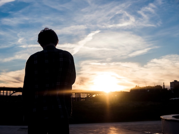 Vue arrière de la silhouette du jeune homme debout et regardant le coucher de soleil