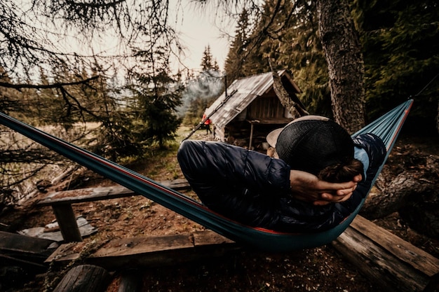 Vue arrière de la silhouette de l'homme relaxant sur un hamac bleu entre les arbres profitant de la vue et du silence dans le paysage des montagnes Forêt brumeuse