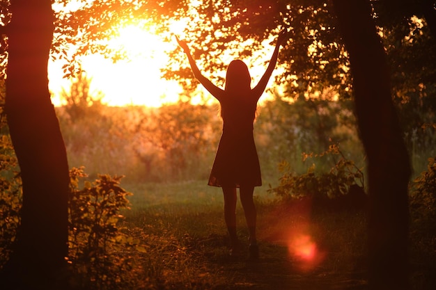 Vue arrière de la silhouette de la jeune femme marchant seule à travers les bois sombres avec les mains tendues en soirée d'été Atteindre votre objectif dans le concept de vie