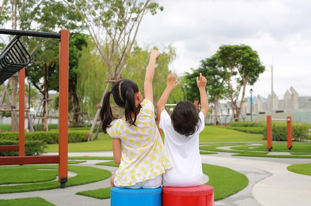 Vue arrière d'une sœur asiatique assise avec son petit frère dans le jardin avec pointant vers le haut dans le parc