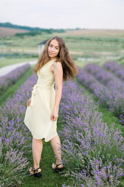 Vue Arrière D'une Superbe Jeune Fille En Robe Jaune Clair Profitant D'une Promenade Dans Un Champ De Lavande En été