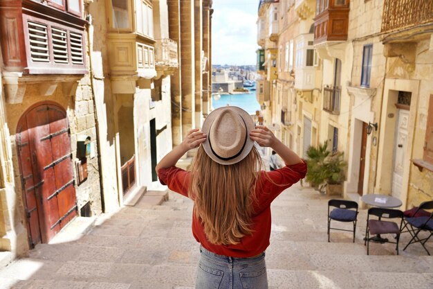 Photo vue arrière d'une touriste tenant un chapeau qui descend les escaliers dans la vieille ville de valletta