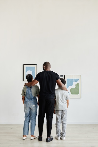 Vue arrière sur toute la longueur de la famille afro-américaine regardant des peintures dans une galerie d'art moderne, espace pour copie