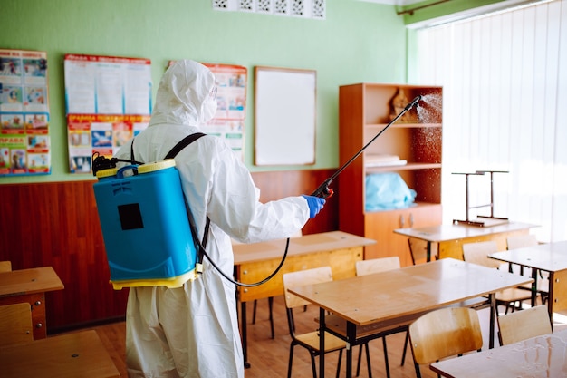 Vue arrière d'un travailleur sanitaire professionnel désinfectant la salle de classe avant le début de l'année scolaire. Un homme portant une combinaison de protection nettoie l'auditorium du coronavirus Covid-19. Soins de santé.