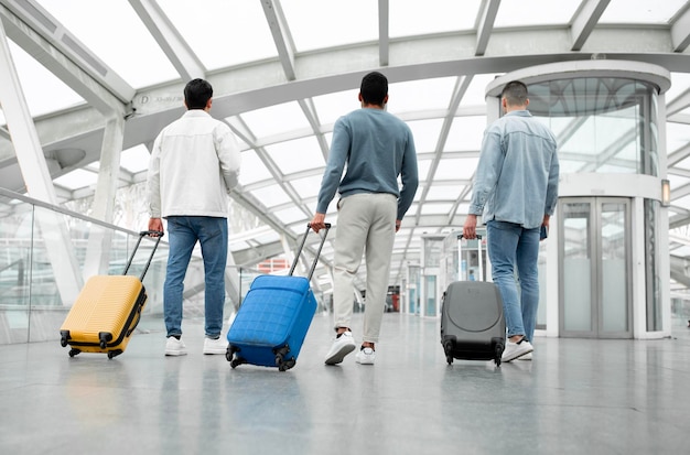 Vue arrière de trois touristes hommes avec bagages à l'aéroport