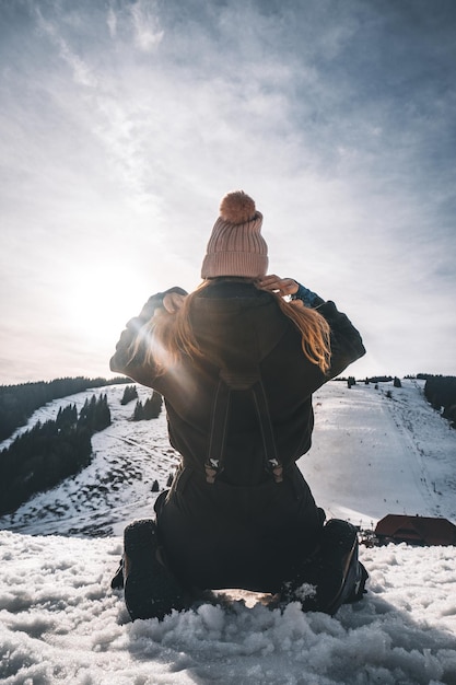 Vue arrière verticale d'une jeune femme portant un chapeau d'hiver à genoux dans la neige