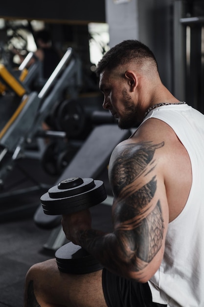 Vue arrière verticale photo recadrée d'un bodybuilder tatoué reposant avec des haltères dans ses mains