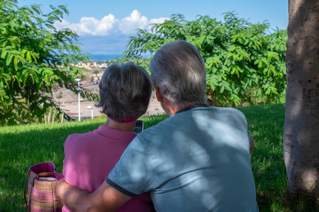 Vue arrière d'un vieux couple de personnes âgées assis dans le pré pendant les vacances d'été embrassant avec amour les personnes âgées profitant de la retraite et d'un mode de vie libre