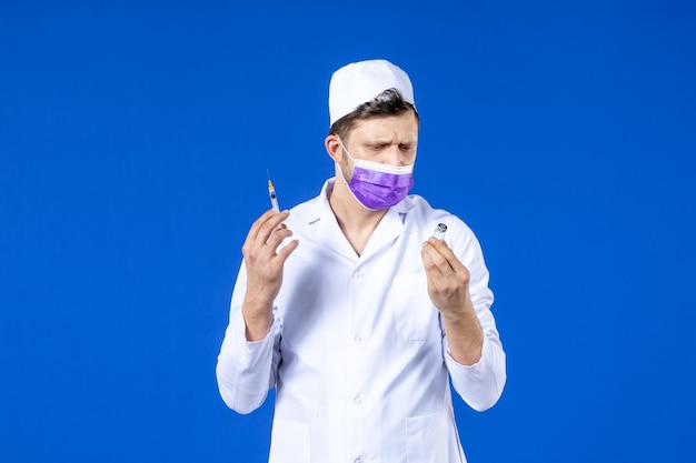 Vue avant du médecin de sexe masculin en costume médical et injection de remplissage de masque avec vaccin sur bleu