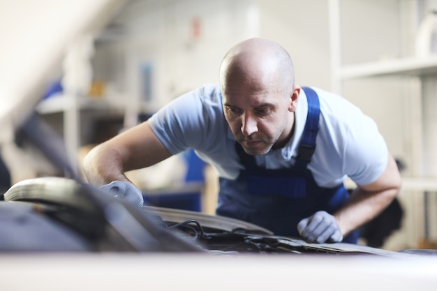 Vue avant portrait de mécanicien automobile musclé à la recherche dans le capot ouvert du véhicule lors de l'inspection dans l'atelier de garage, espace copie