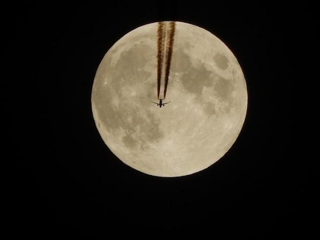 Photo vue à bas angle d'un avion volant contre la lune la nuit