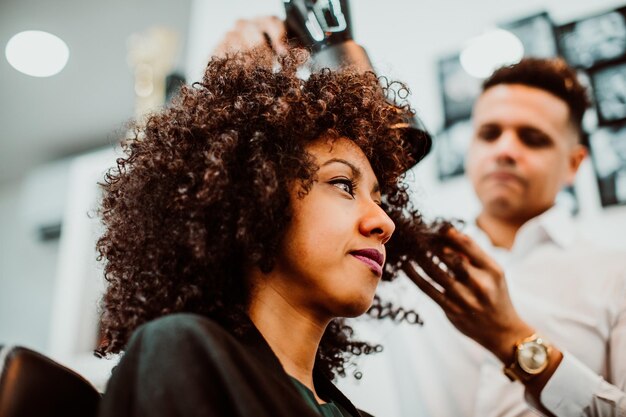 Photo vue à bas angle du coiffeur séchant les cheveux d'une femme dans un salon