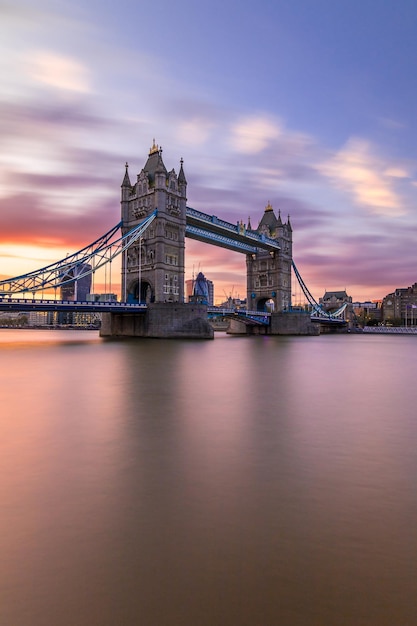 Vue à bas angle du pont de la tour sur la rivière contre un ciel nuageux au coucher du soleil