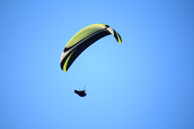 Photo vue à bas angle d'une femme en parapente contre un ciel bleu clair
