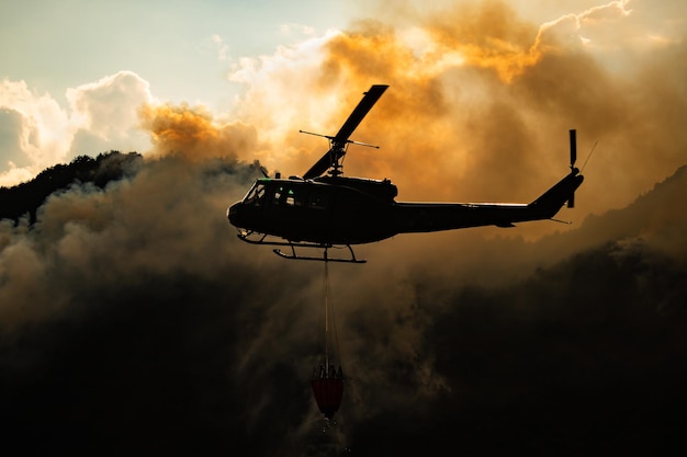 Vue à bas angle de l'hélicoptère de silhouette contre la fumée pendant le coucher du soleil