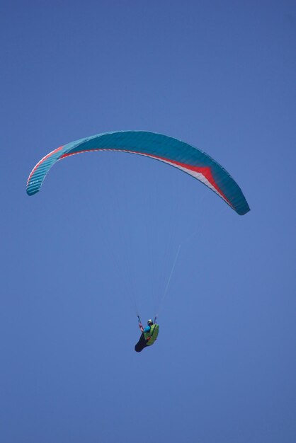 Photo vue à bas angle d'une personne en parapente contre un ciel bleu clair