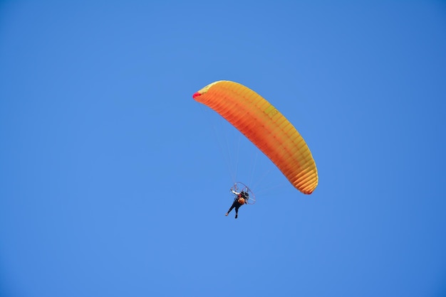Photo vue à bas angle d'une personne en parapente contre un ciel bleu clair