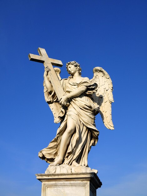 Photo vue à bas angle de la statue d'ange avec la croix contre un ciel clair