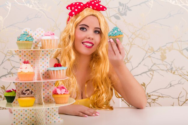 Vue d&#39;une belle fille blonde pin-up avec des cupcakes colorés sur une table.