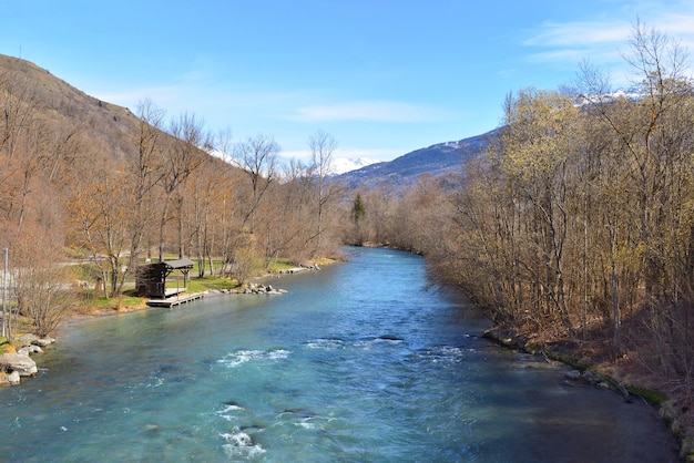 Vue sur la belle rivière alpine bleue qui coule entre la rive de la forêt et le fond de la montagne enneigée au printemps