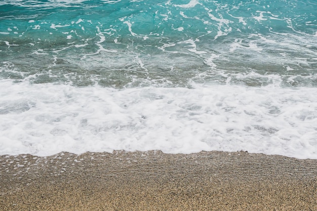 vue sur le bord de mer avec des pierres et du sable, des vagues douces avec de l'écume, de l'eau bleue et turquoise