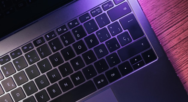 Vue de bureau du clavier d'ordinateur portable avec des lumières violettes sur une table en bois. Lieu de travail. Travail à domicile.