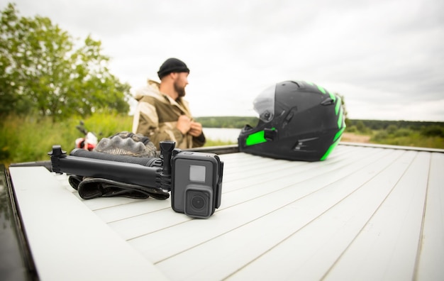 Photo vue de la caméra de sport avec support à côté du casque de moto au premier plan et de l'homme sur le fond panoramique