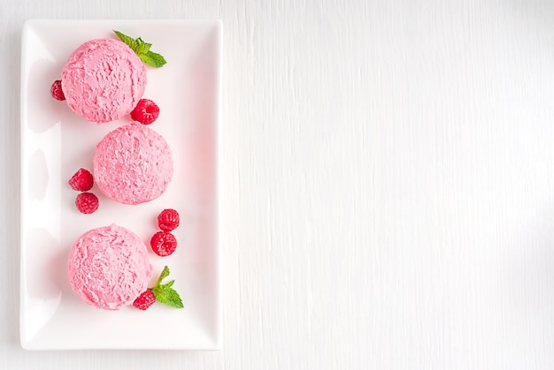 Vue ci-dessus des boules de crème glacée rose aux baies congelées avec des framboises et des feuilles de menthe sur une assiette sur la table