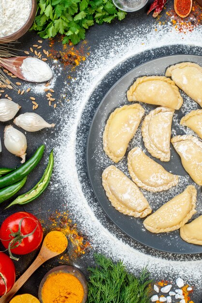 Vue ci-dessus des boulettes crues sur une assiette grise avec de la farine autour et divers aliments sur une surface noire