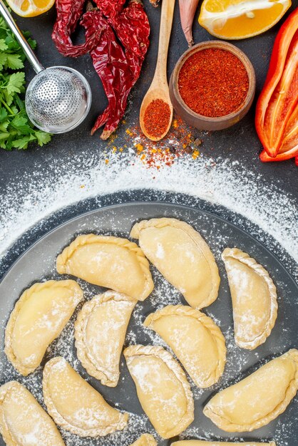 Vue ci-dessus des boulettes crues sur une assiette grise avec de la farine autour et divers aliments sur un tableau noir