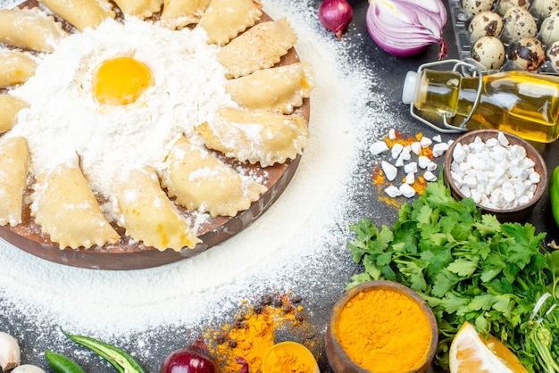 Vue ci-dessus de boulettes crues à bord autour de la farine et d'un ensemble d'aliments sur une surface de couleur sombre